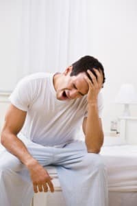 A man yawning on the bed - possibly suffering insomnia.