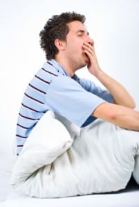 Yawning young man on bed in need of sleep therapy treatment