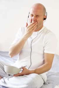 Yawning man with headphones on having breakfast in bed - he needs sleep therapy